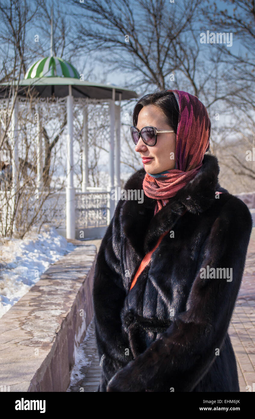 A woman in sunglasses wearing a black fur coat looks into the distance Stock Photo