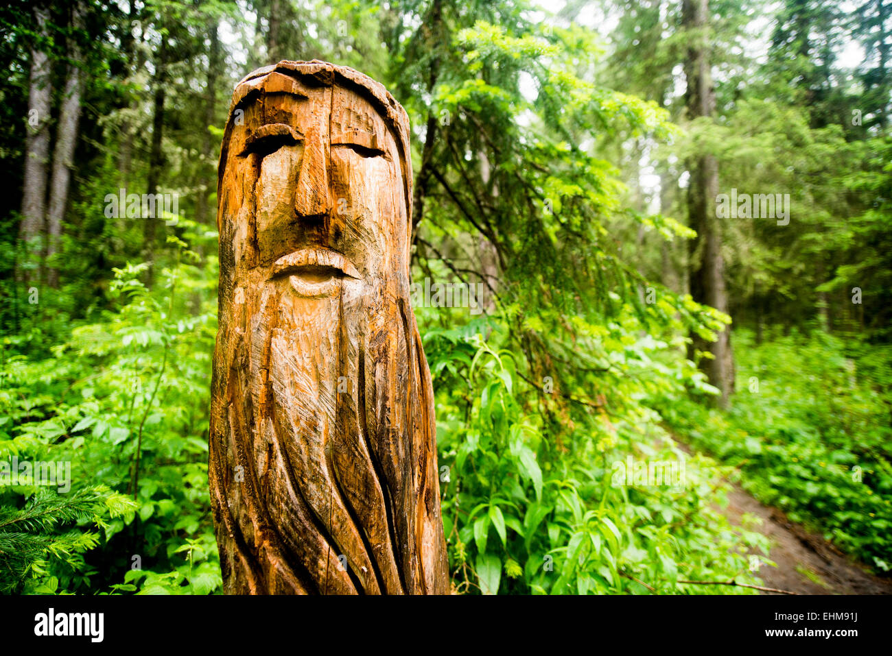 Close up of carved totem pole near forest path Stock Photo
