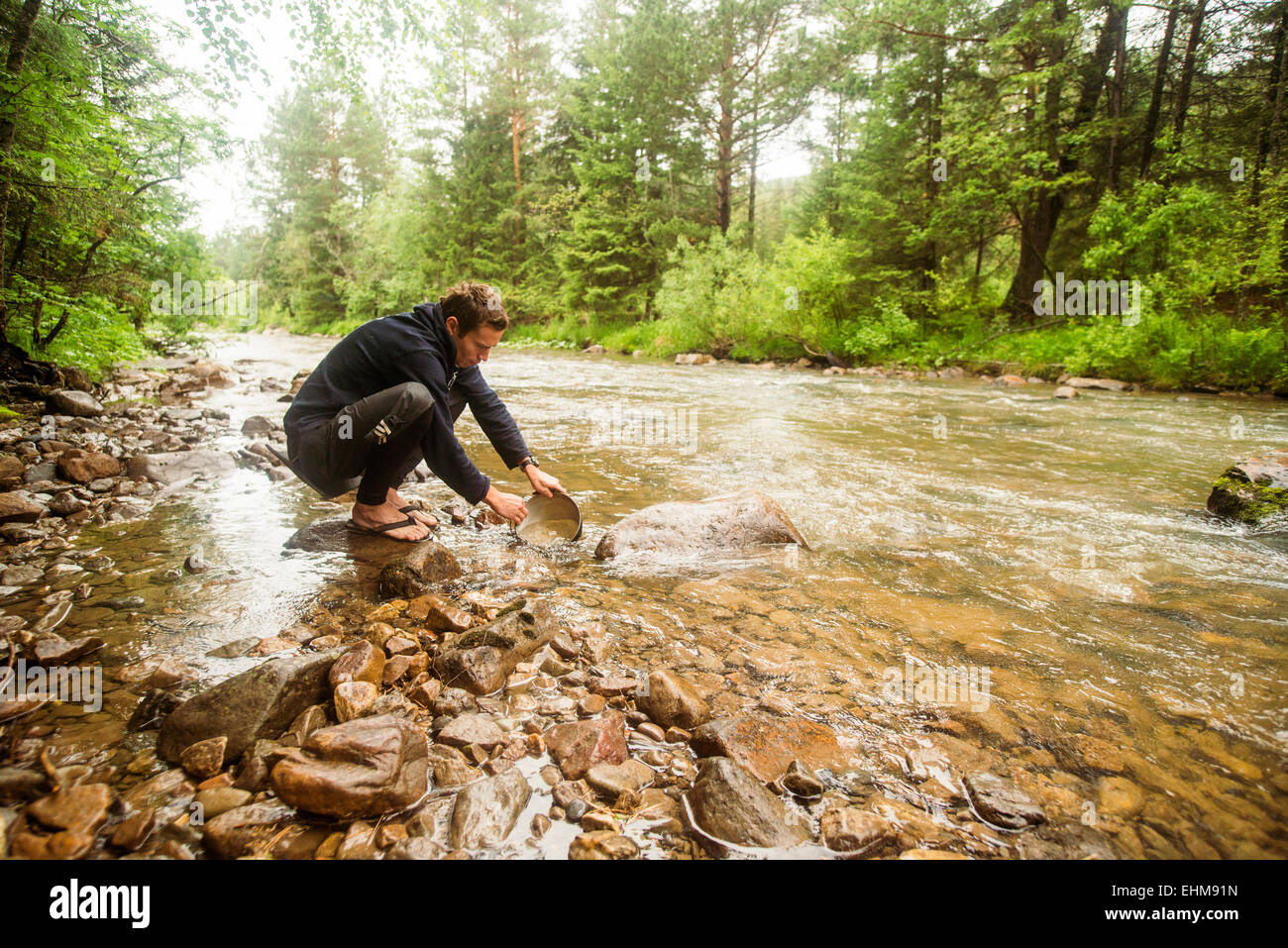 Caucasian man crouching in forest river Stock Photo