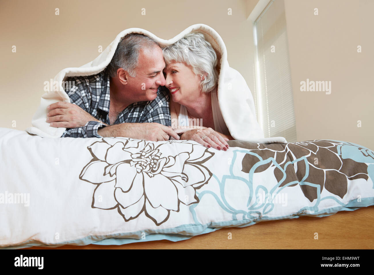 Older couple rubbing noses under blanket on bed Stock Photo