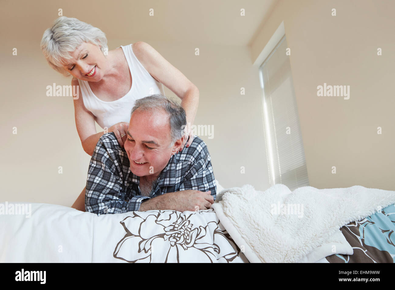 Older woman giving husband back massage on bed Stock Photo