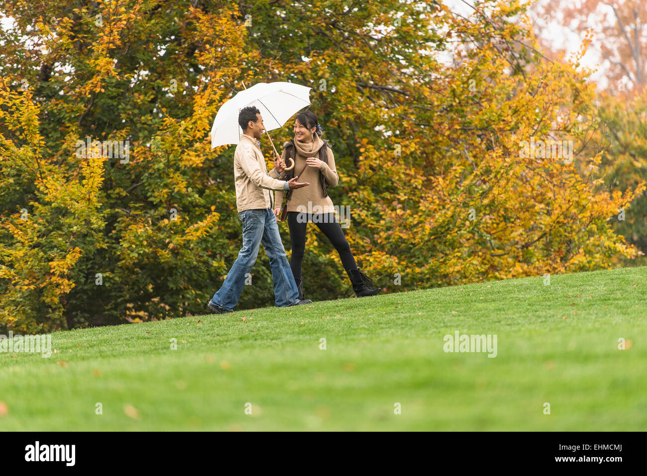 Couple walking with umbrella in park Stock Photo