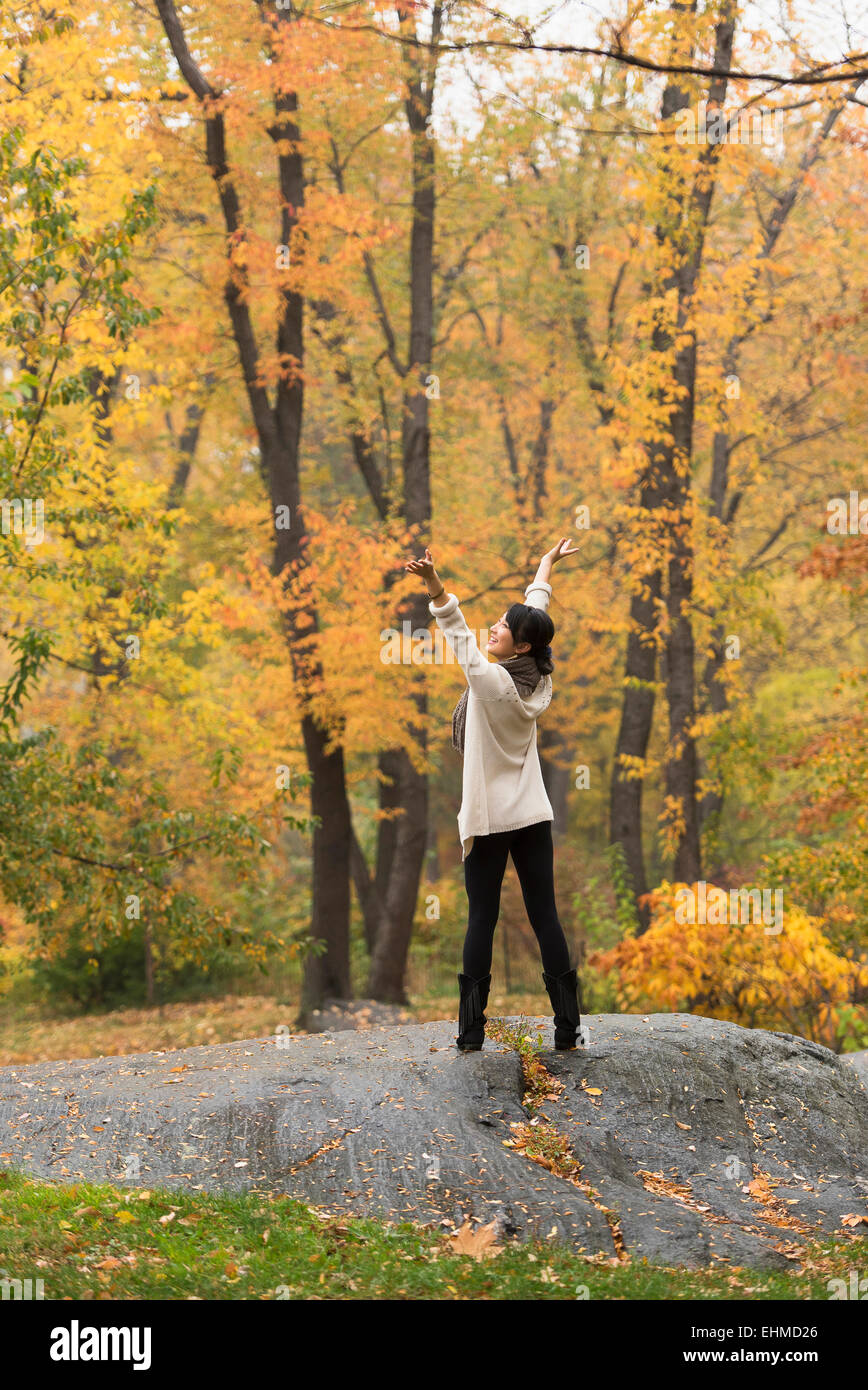 Asian woman cheering with arms outstretched on rock in park Stock Photo