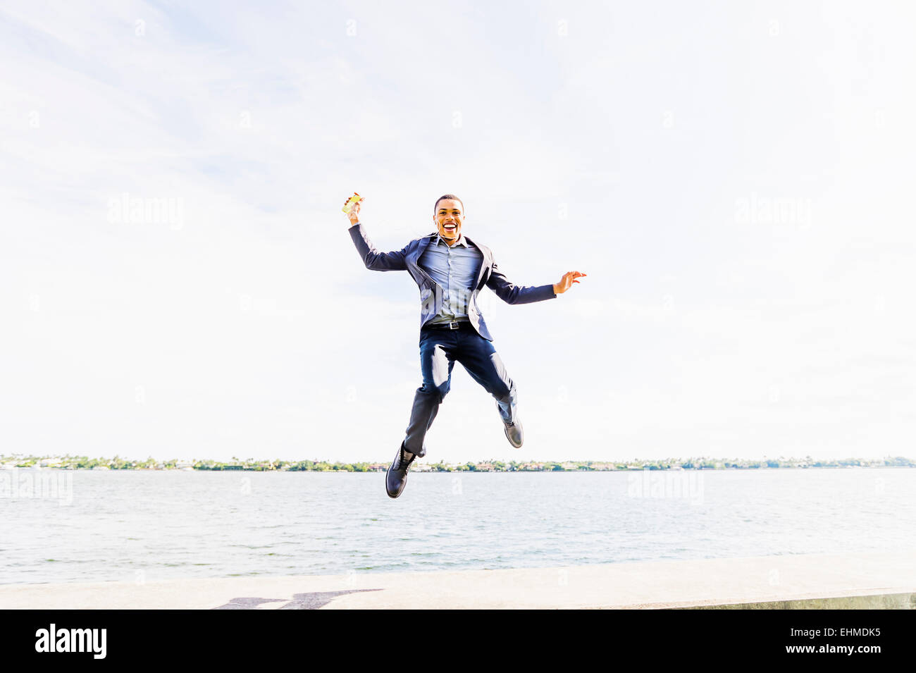 Black businessman jumping for joy at waterfront Stock Photo