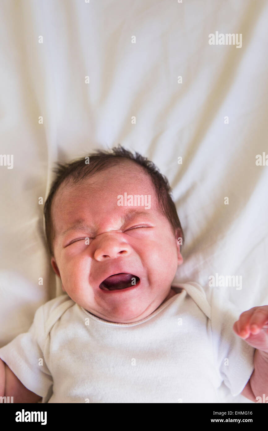 Close up of mixed race baby crying on bed Stock Photo