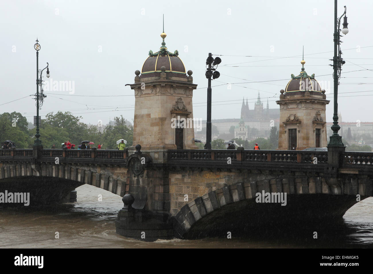 People observe the rising water from the Legion Bridge partially flooded by the swollen Vltava River in Prague, Czech Republic. Prague Castle and St Vitus' Cathedral are seen in the background. Stock Photo