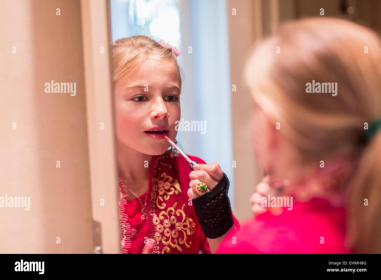 Caucasian girl applying lip gloss in mirror Stock Photo