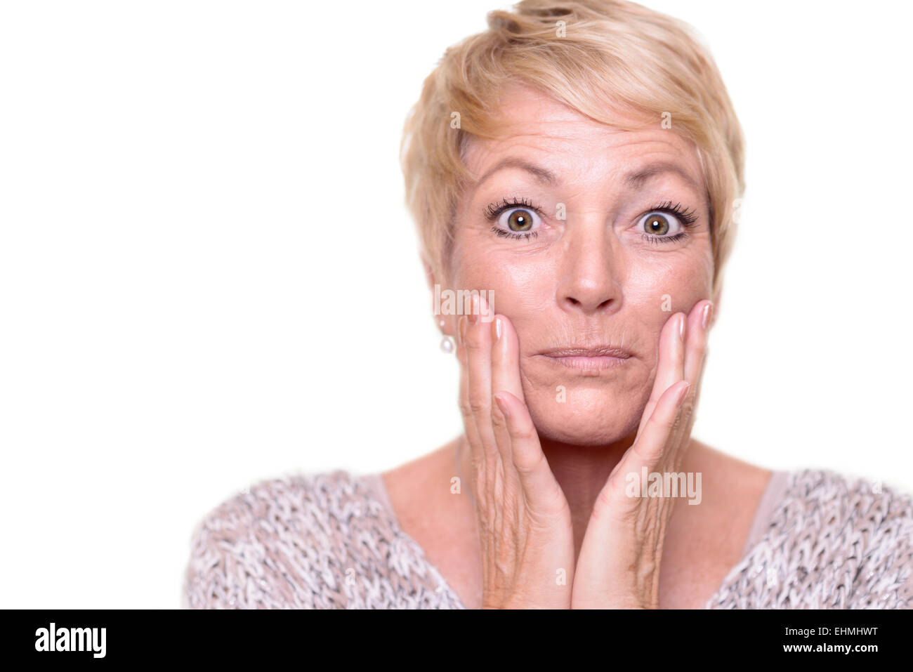 Attractive senior blond woman with a wide-eyed expression and her glasses on her head checking her complexion Stock Photo
