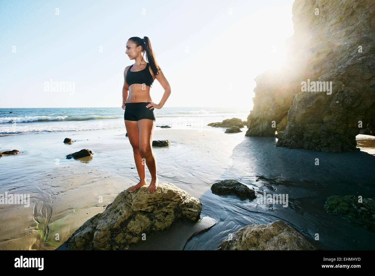 Mixed race woman standing on rock on beach Stock Photo