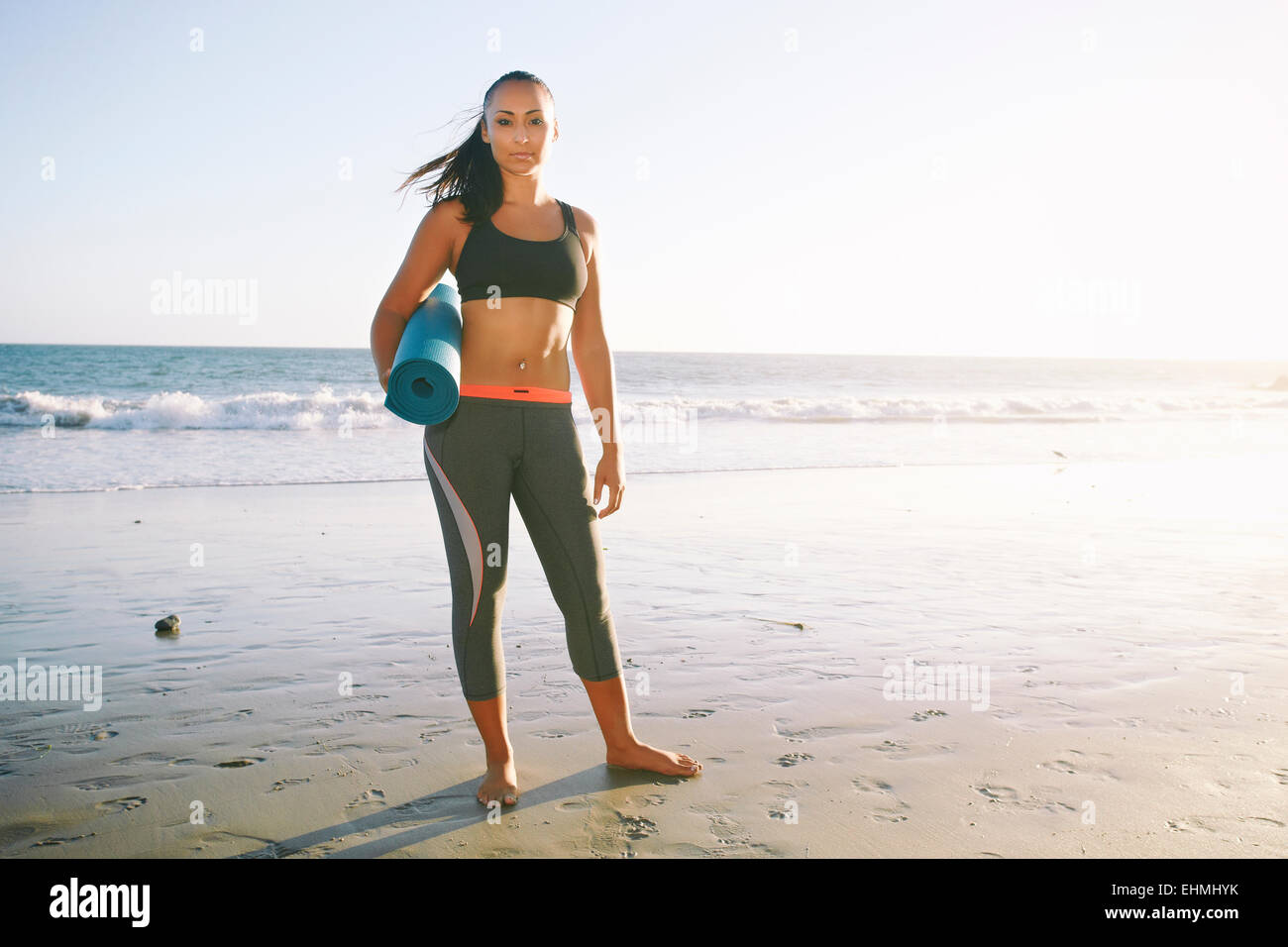 Mixed race woman holding yoga mat on beach Stock Photo