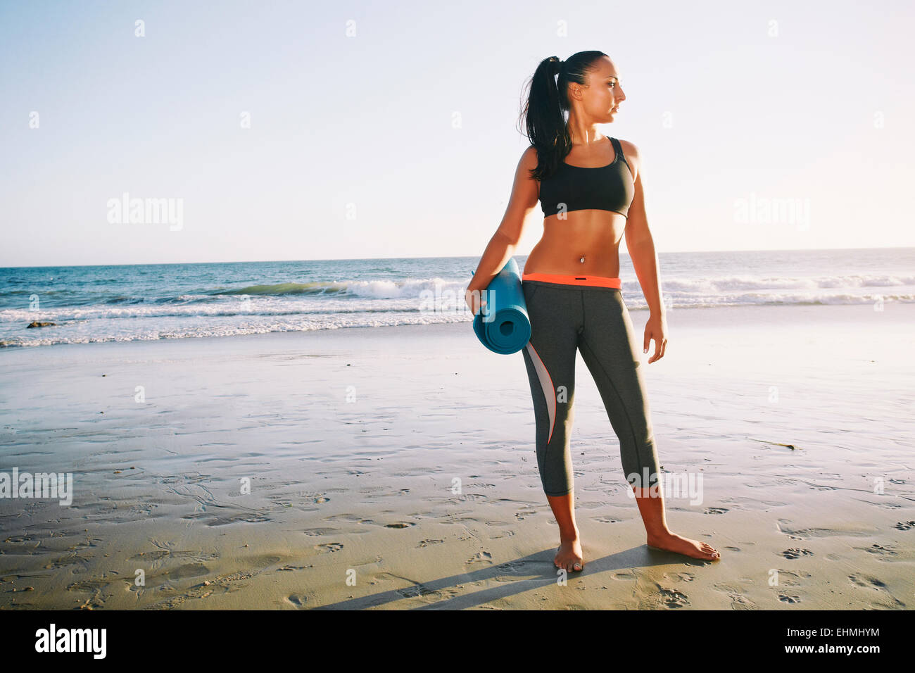 Mixed race woman holding yoga mat on beach Stock Photo