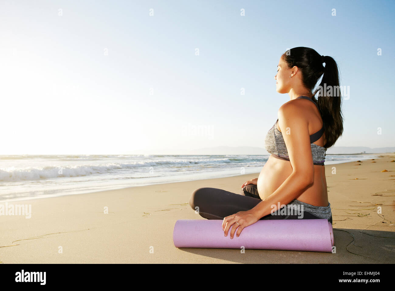 Pregnant Hispanic woman meditating on beach Stock Photo