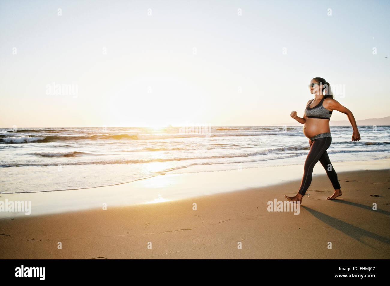Pregnant Hispanic woman walking on beach Stock Photo