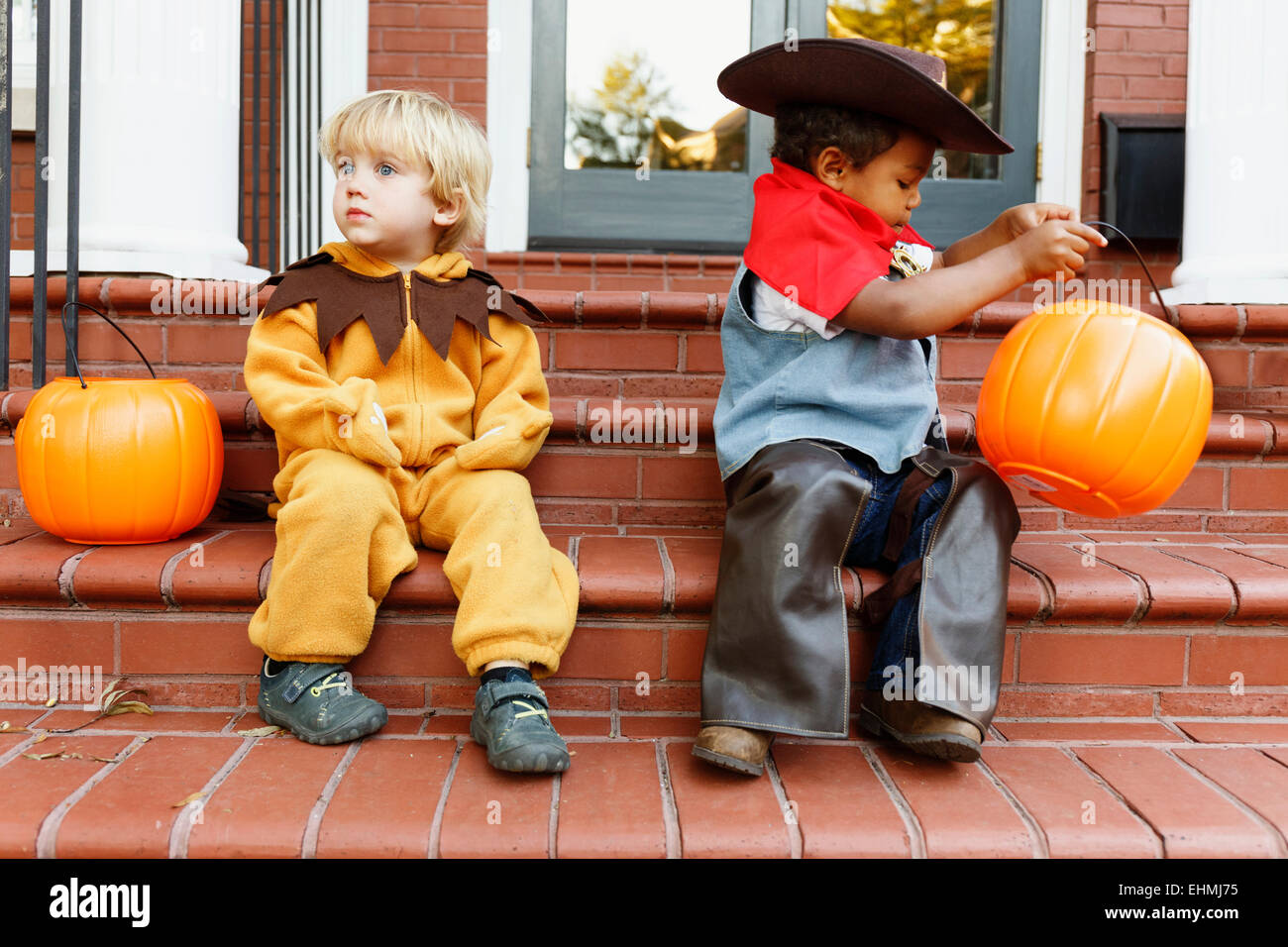 Boys in costumes trick sitting on front stoop on Halloween Stock Photo