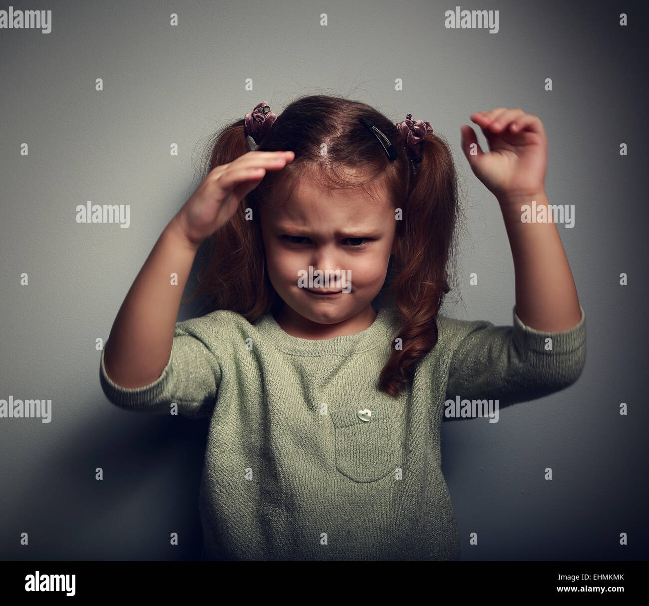 Very angry kid girl looking aggressive and waving the arms on dark background. Closeup portrait Stock Photo