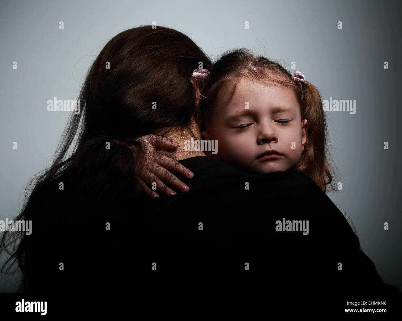 Sad crying daughter hugging her mother with sad face on dark shadows background Stock Photo