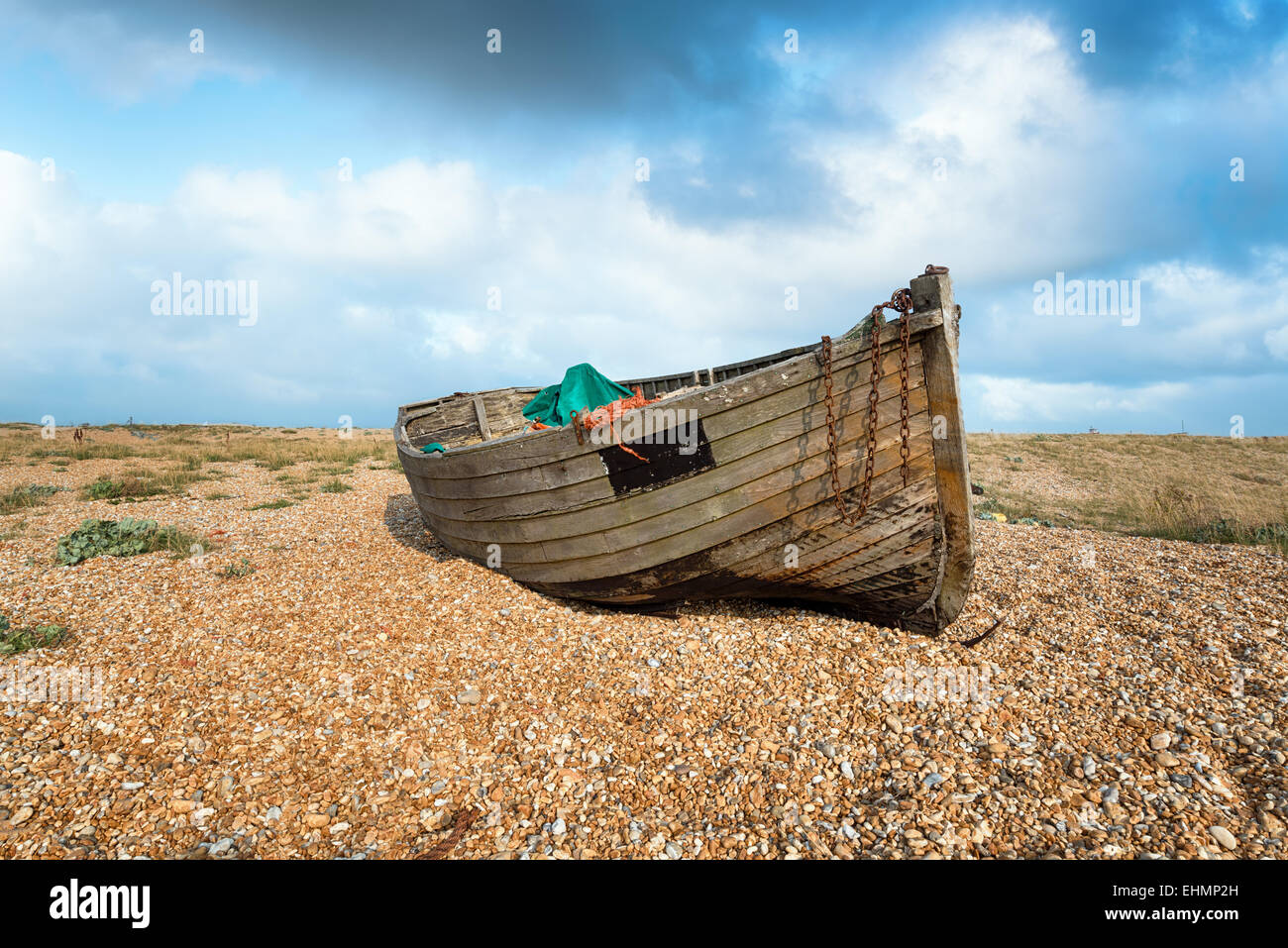 An old weathered wooden fishing boat on a pebble beach under a blue sky ...