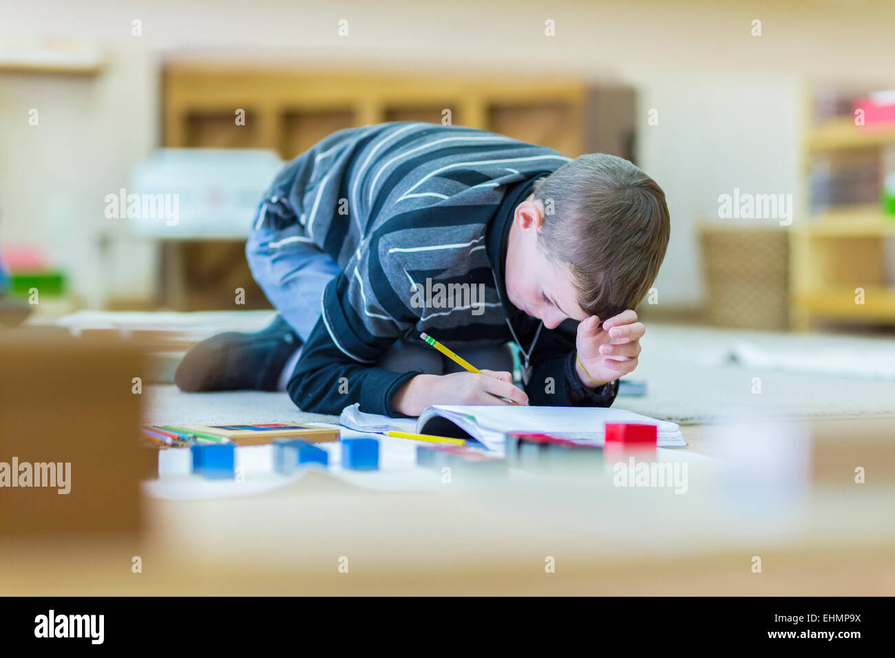 Caucasian boy writing in notebook on floor in classroom Stock Photo