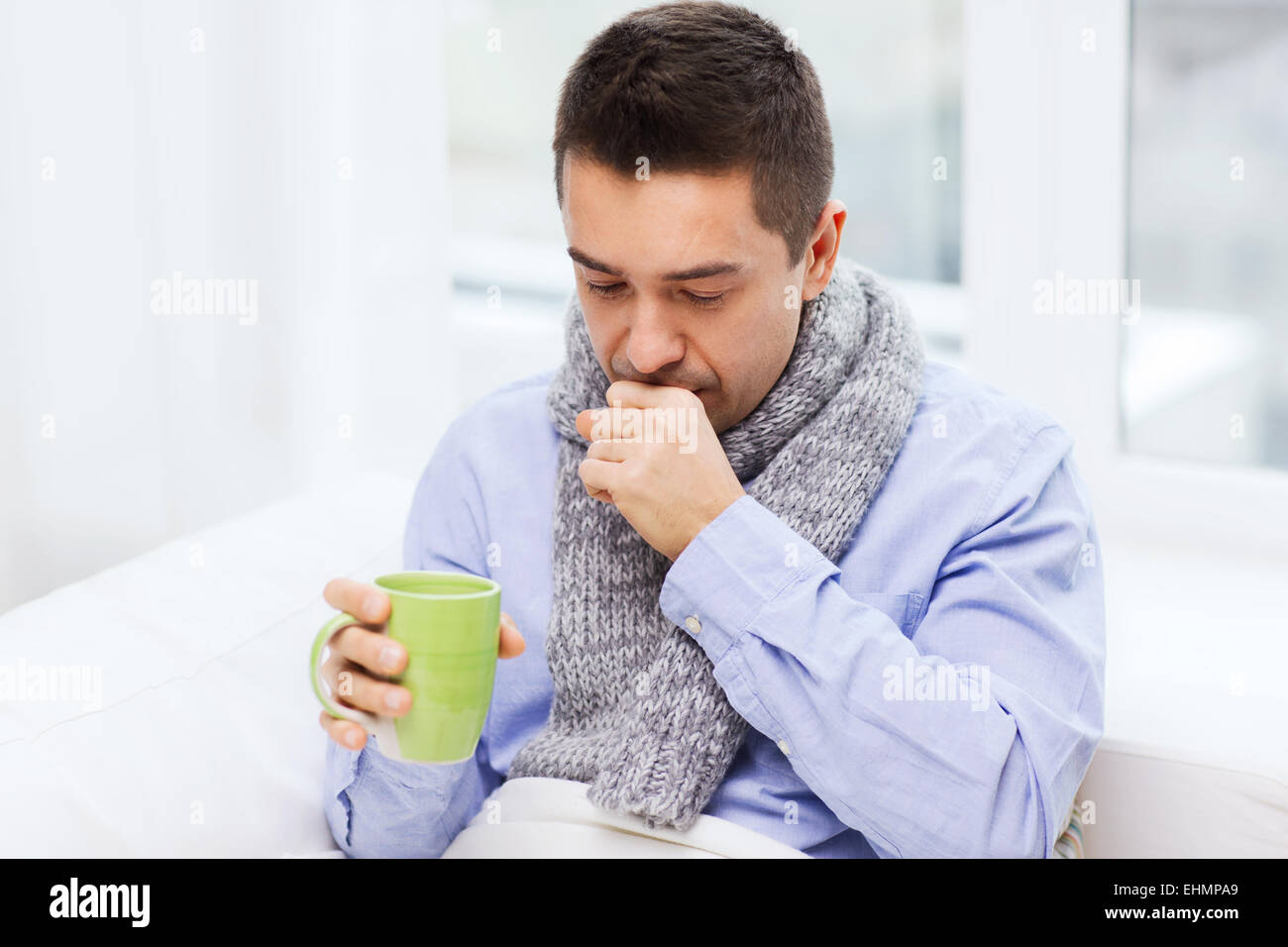 ill man with flu drinking tea and coughing at home Stock Photo