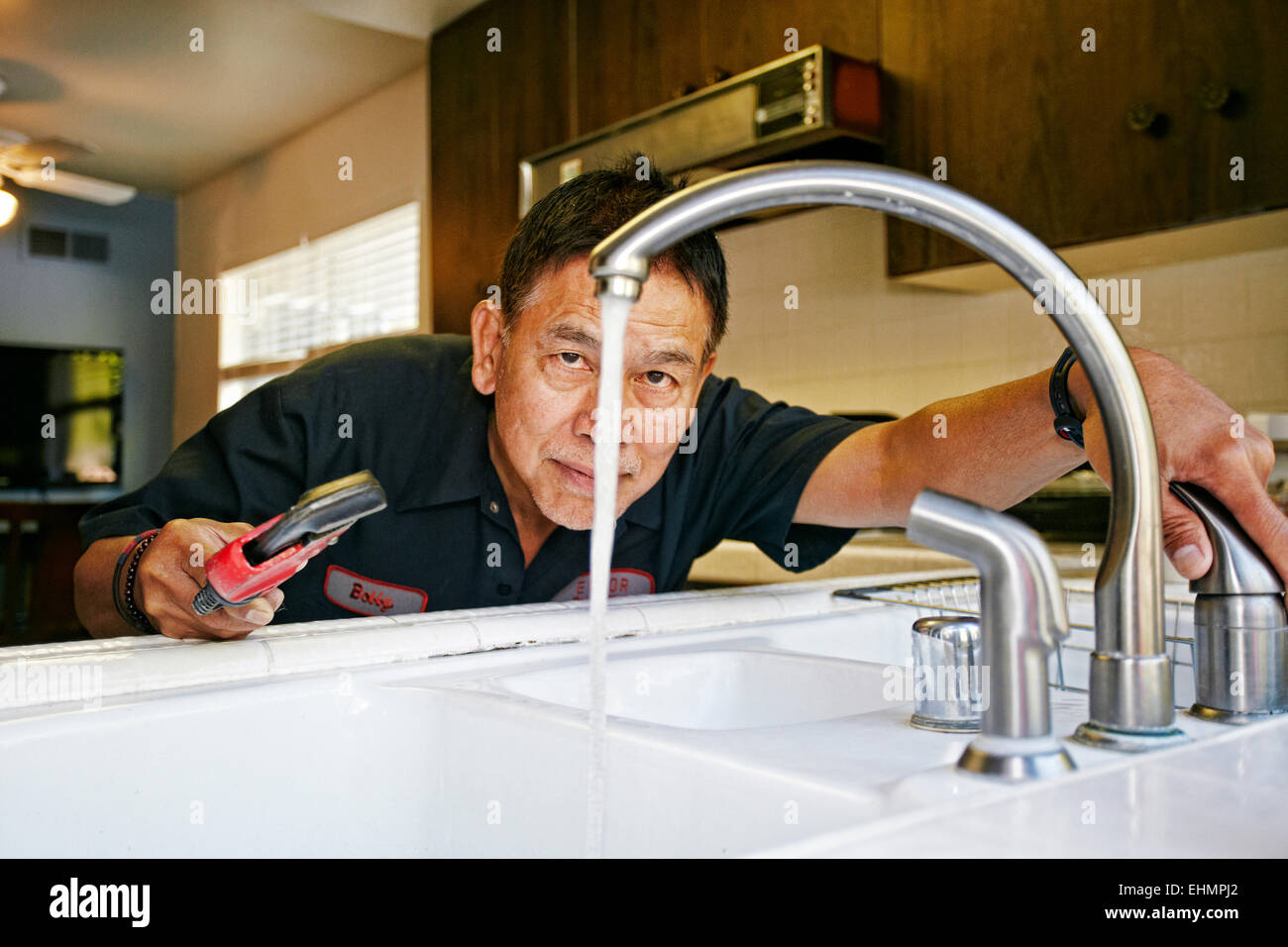 Pacific Islander plumber examining sink in kitchen Stock Photo