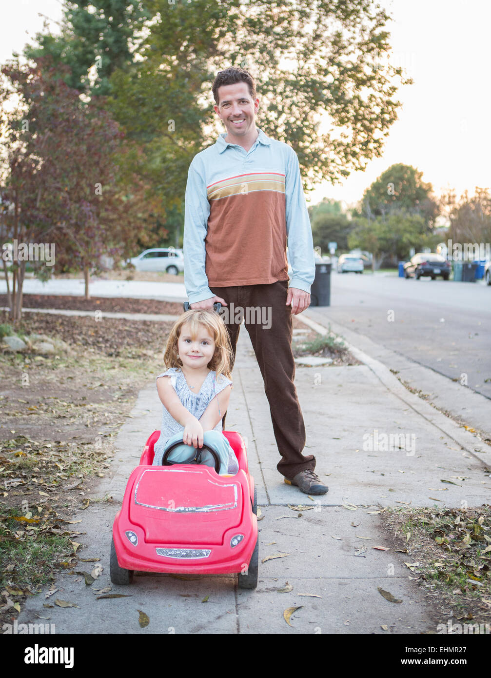Caucasian father pushing daughter in toy car Stock Photo