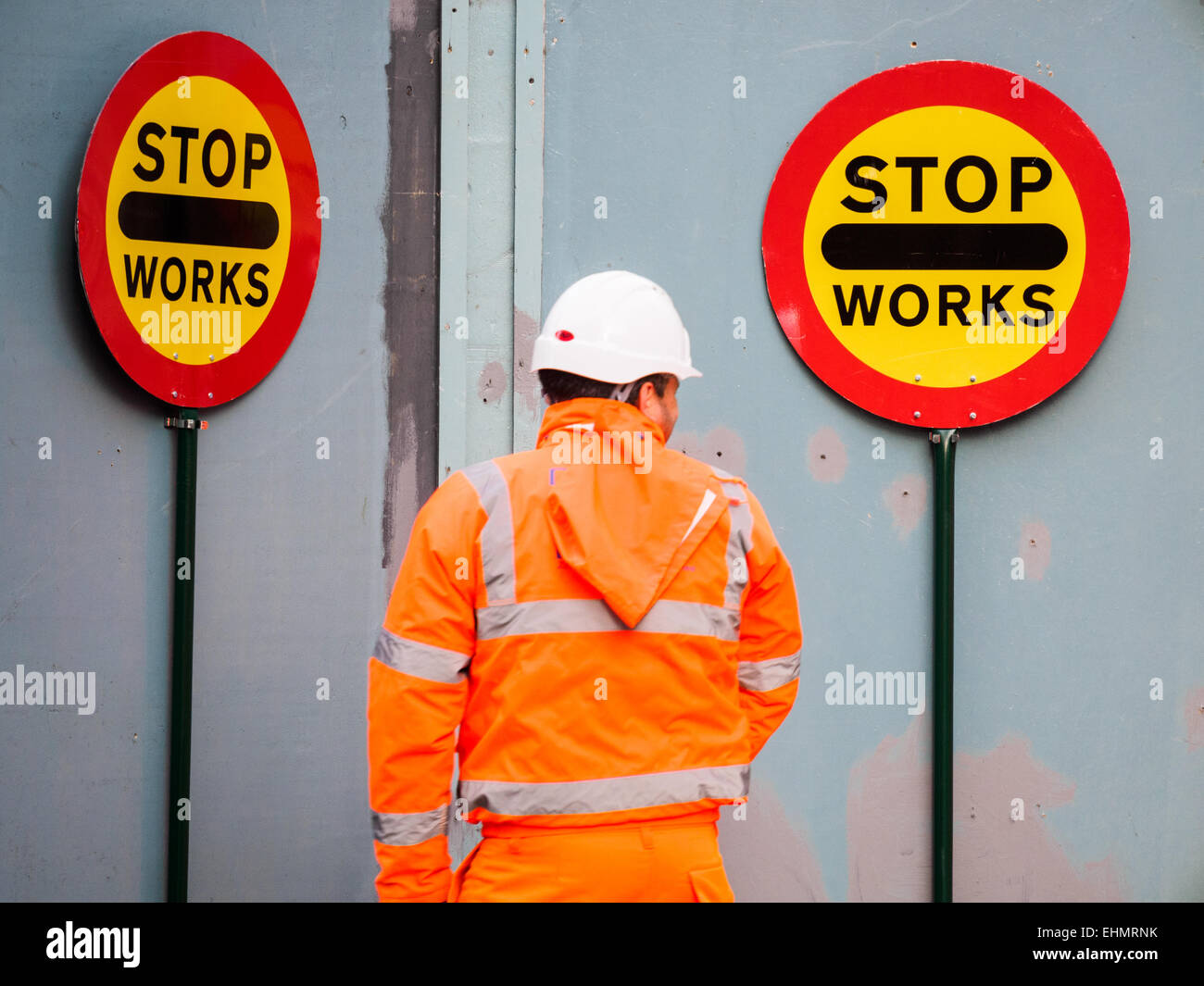 A builder walks by some hand-held traffic control signs in London UK Stock Photo