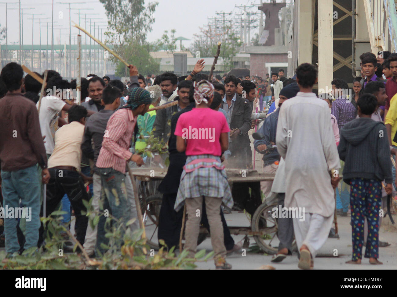 Lahore, Pakistan. 15th March, 2015. People around bringing small sticks and halt other vehicles to pass the way. There are bunch of Pakistani gather around the burning bodies of what the mob called suspects in aiding the suicide bombers nearby the scene of an attack on a church, killing at least 11 worshipers and wounding several others, officials said, in the latest attack against religious minorities. An angry mob later lynched two people they accused of aiding the suicide bombers outside the churches, a spokesman for the provincial government said. Credit:  PACIFIC PRESS/Alamy Live News Stock Photo