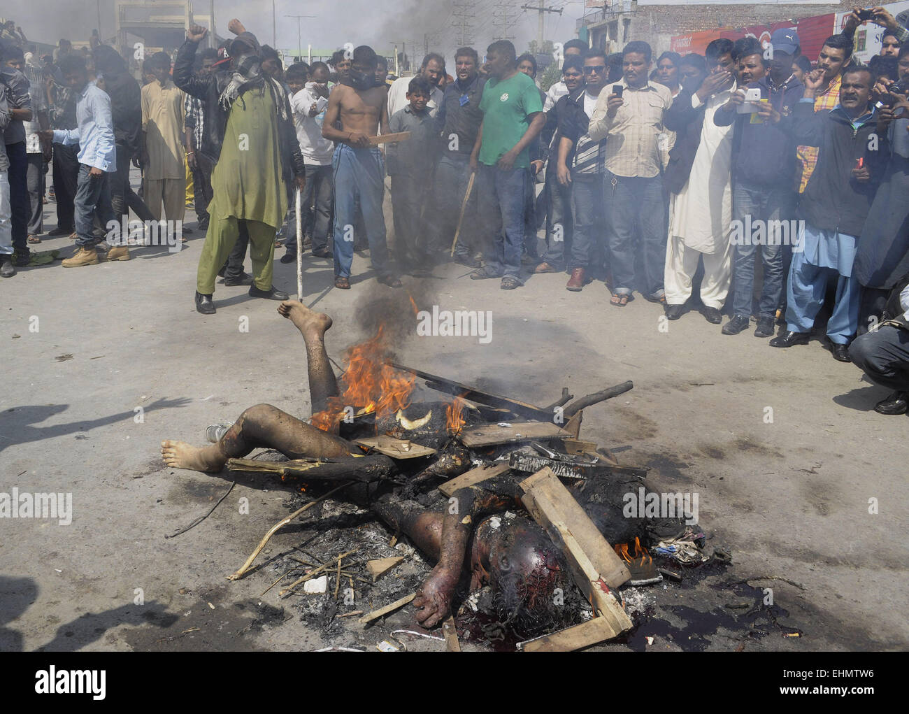 Lahore, Pakistan. 15th March, 2015. People gather around the burning bodies of what the mob called suspects in aiding the suicide bombers nearby the scene of an attack on a church in Lahore, Pakistan, 15 March 2015. Two Taliban suicide bombers blew themselves up outside two churches in the impoverished Yohana Abad sector of eastern Lahore during Sunday mass, killing at least 11 worshippers and wounding several others, officials said, in the latest attack against religious minorities. Credit:  PACIFIC PRESS/Alamy Live News Stock Photo