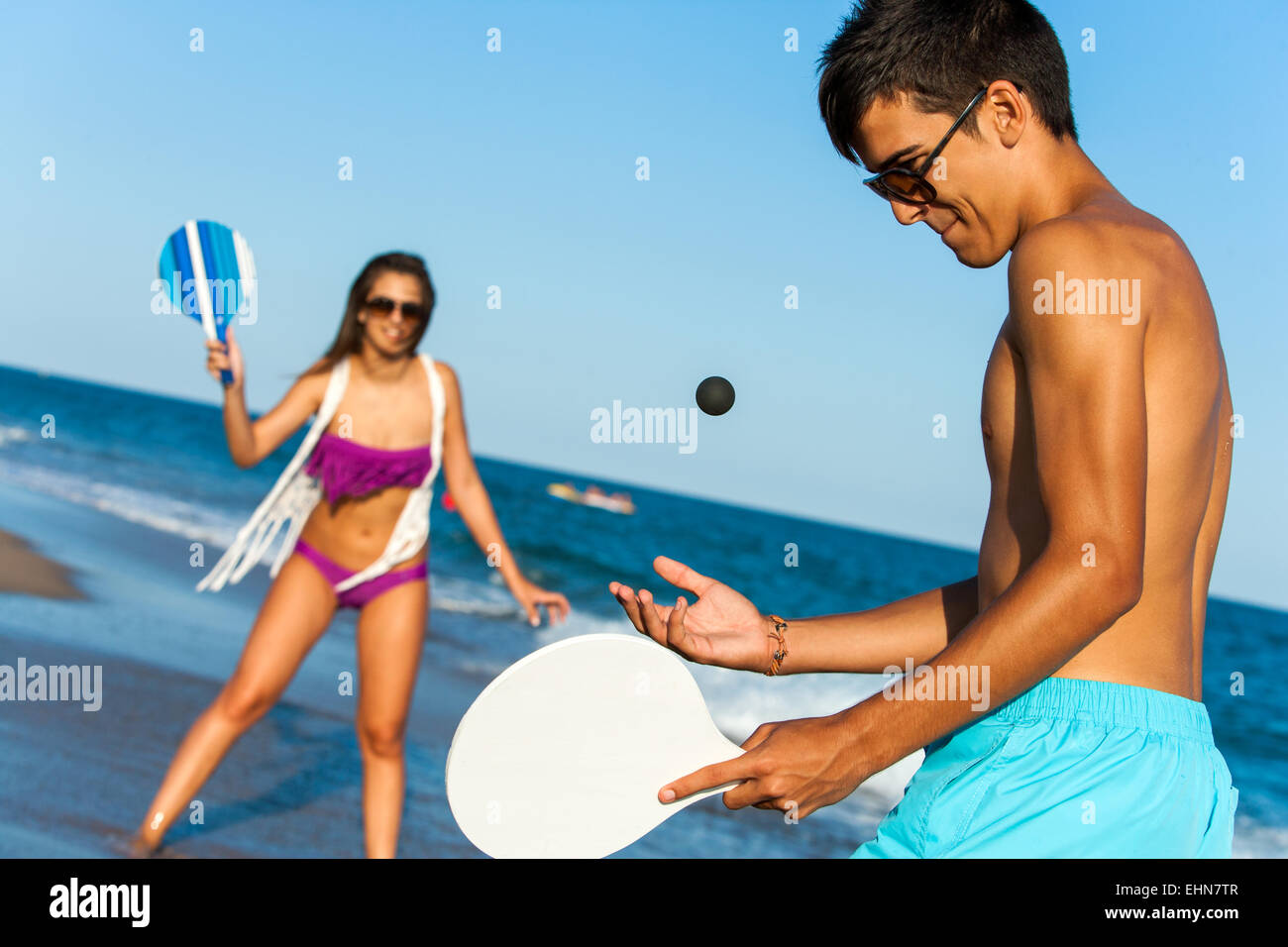 Teen couple in swim wear playing smash ball beach tennis outdoors. Stock Photo