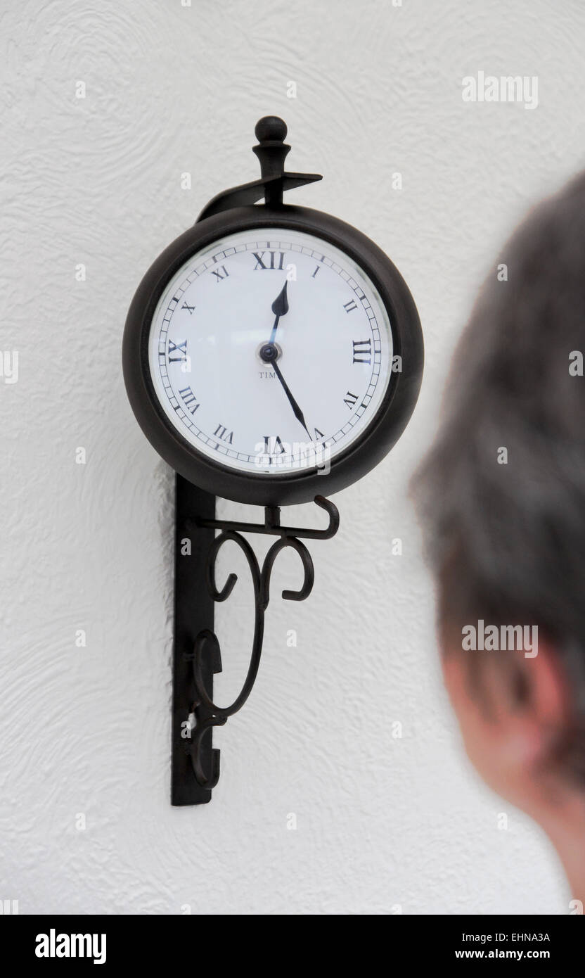 Old lady female pensioner looking at clock on wall to tell the time Stock Photo