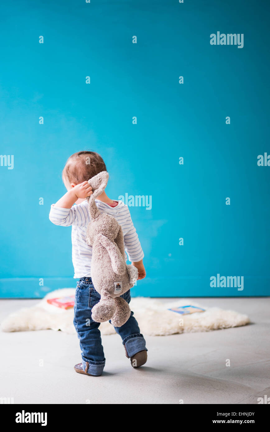 Toddler walking away from camera with rabbit toy over shoulder Stock Photo