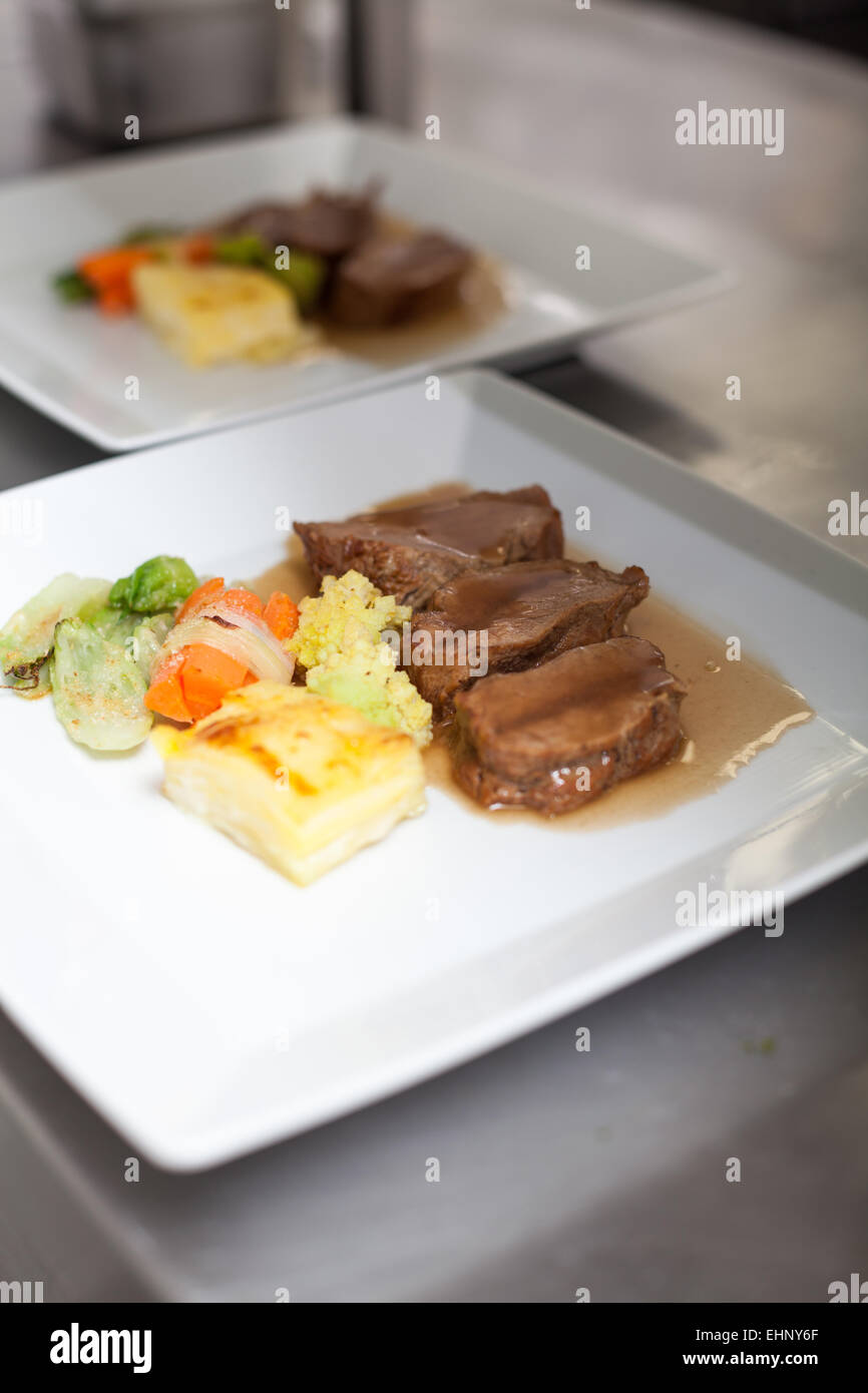 Chef plating up food in a restaurant pouring a gravy or sauce over the meat before serving it to the customer, close up view of Stock Photo