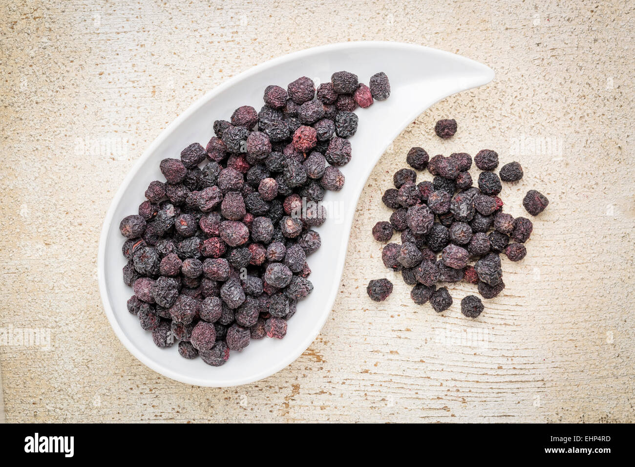 Dried chokeberry (aronia berry) in a teardrop shaped bowl against rustic barn wood Stock Photo