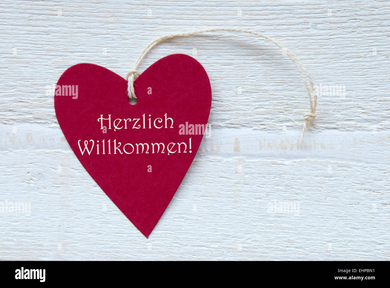 One Red Heart Label Or Tag With White Ribbon On White Wooden Background With German Text Herzlich Willkommen Means Happy Welcome Stock Photo
