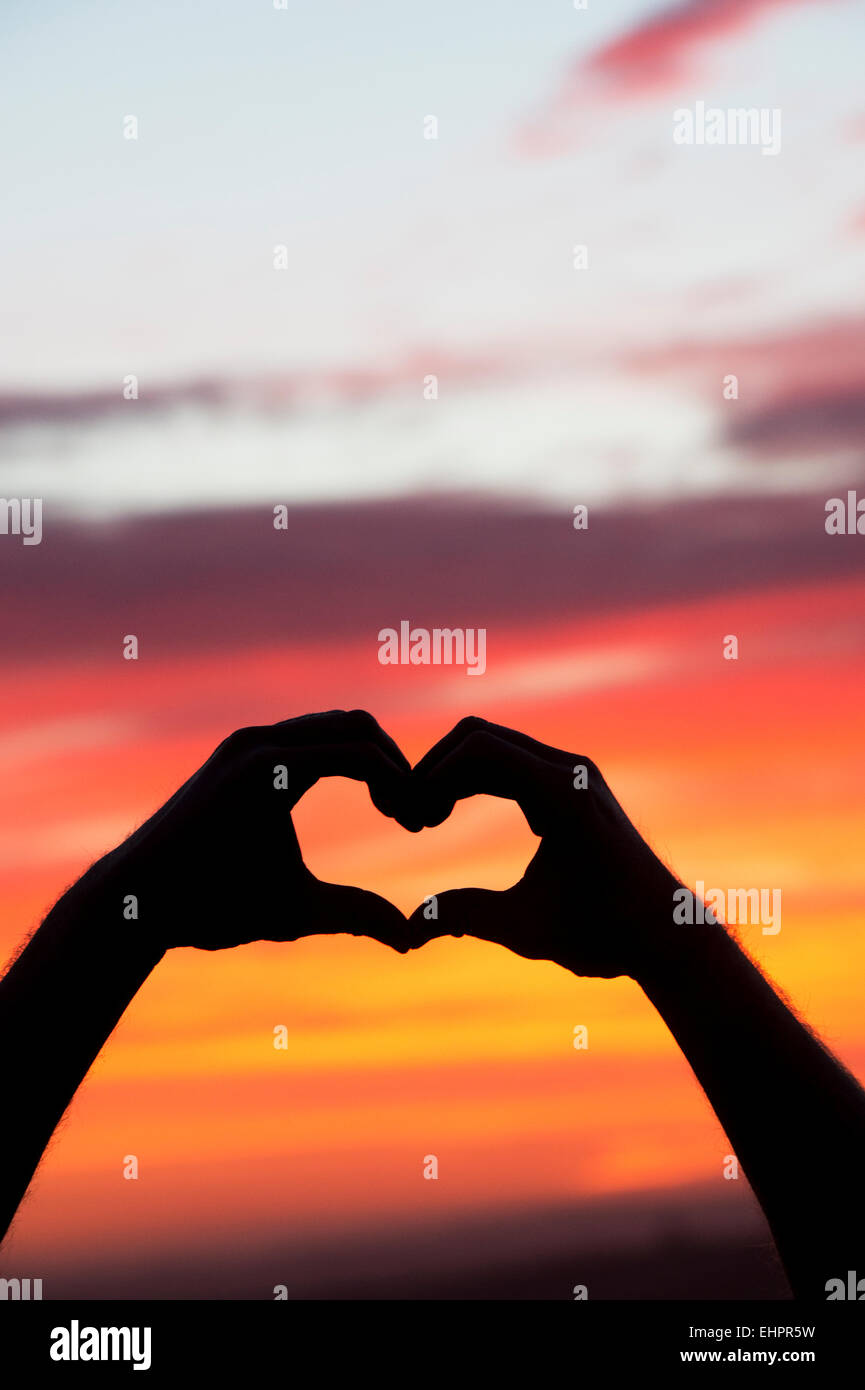 Heart hands gesture at sunrise. Silhouette Stock Photo