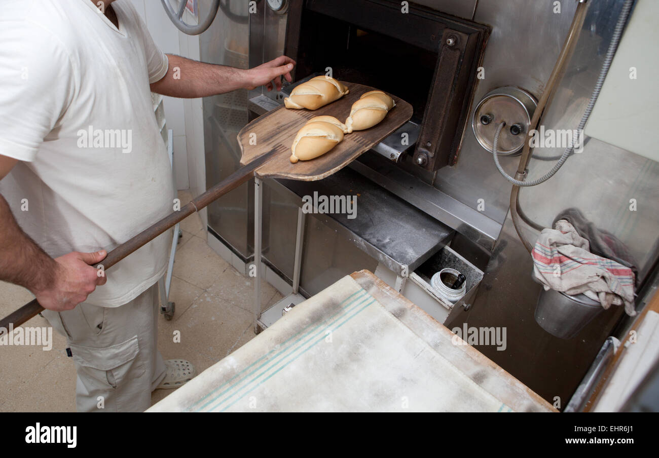 Baker taking fresh baked bread from oven. Manufacturing process of