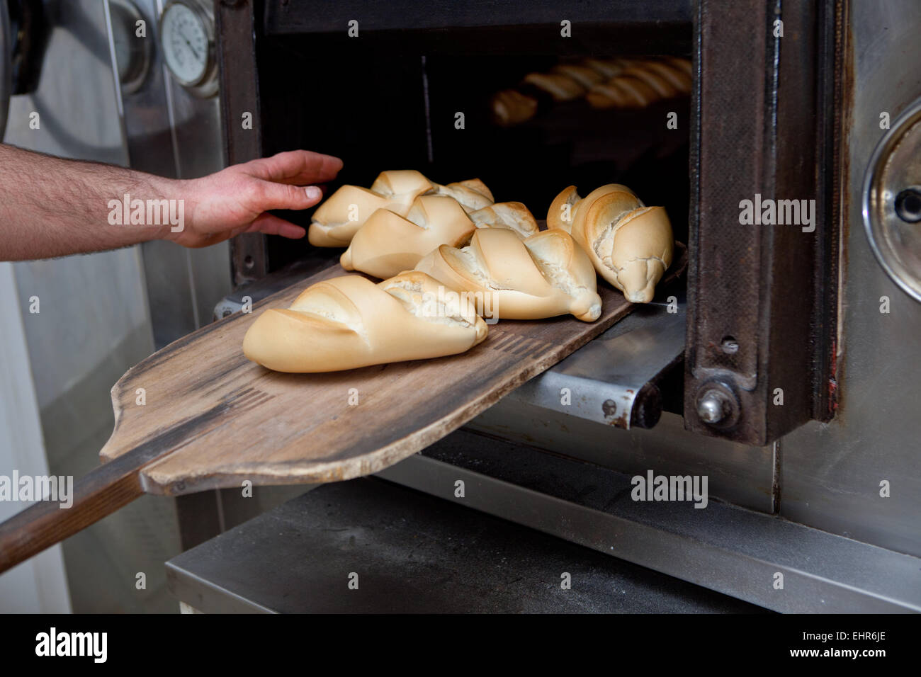 Baker taking fresh baked bread from oven. Manufacturing process of