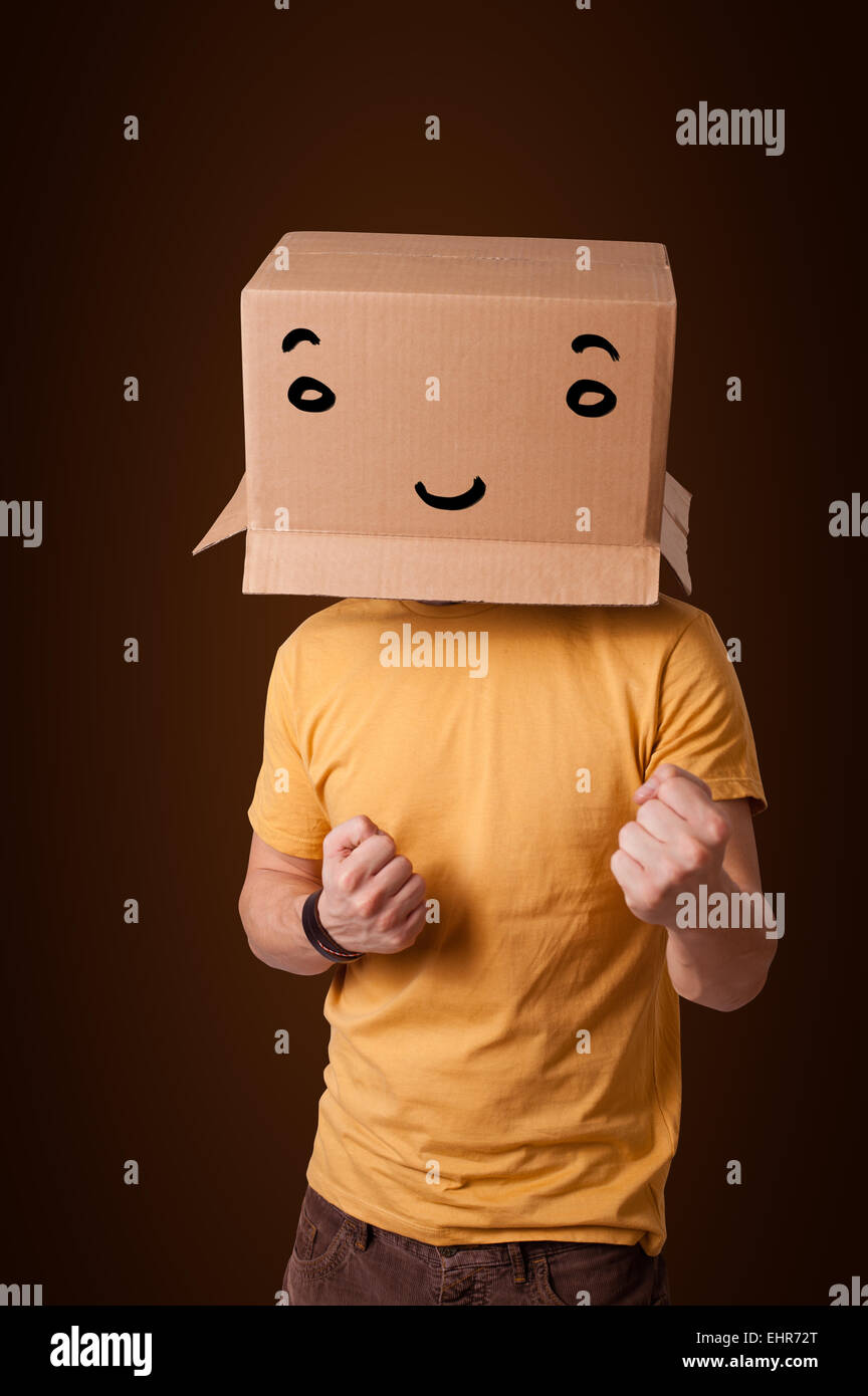 Young man gesturing with a cardboard box on his head with smiley face ...