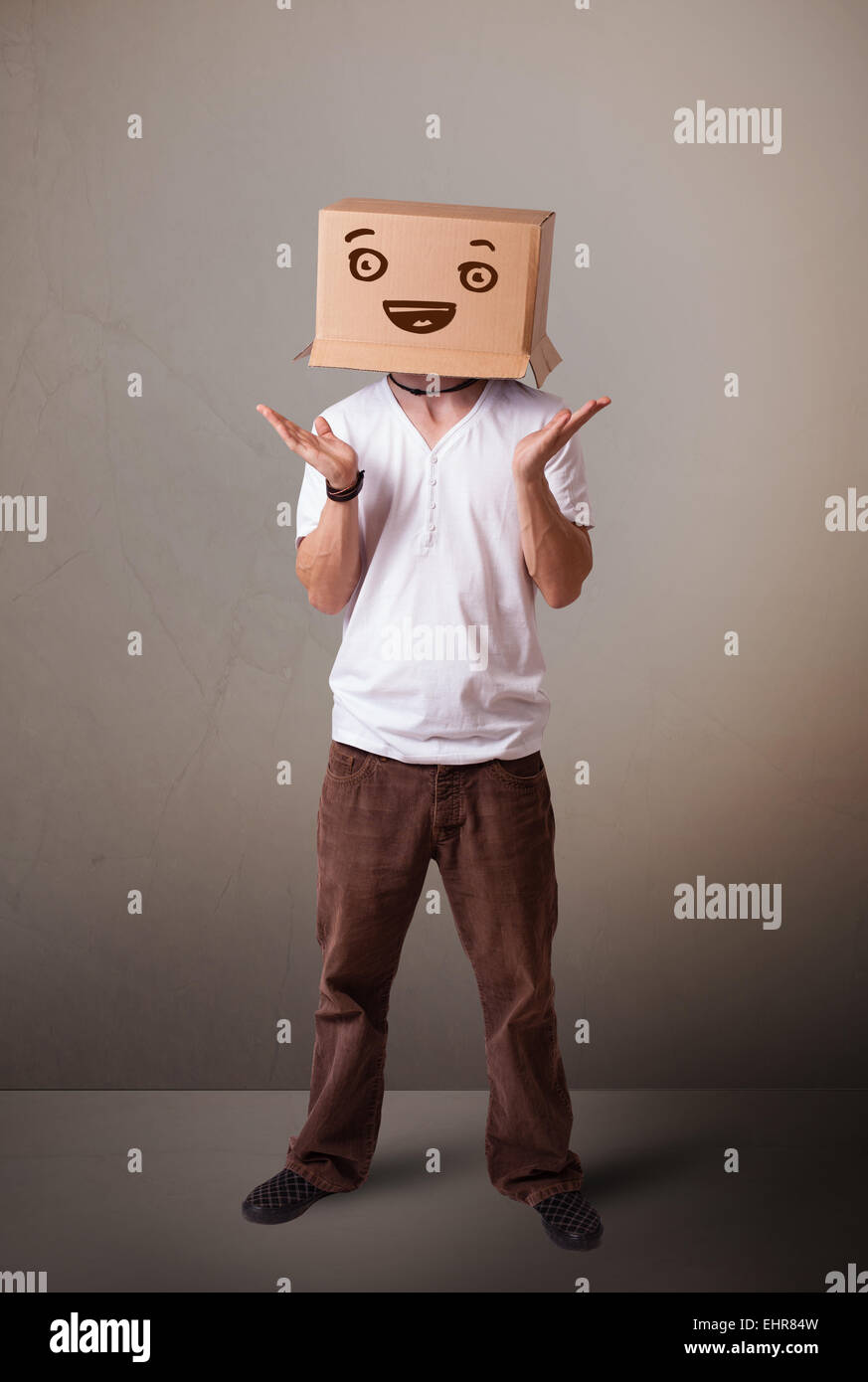 Young man gesturing with a cardboard box on his head with smiley face ...