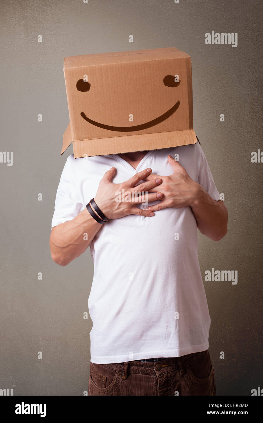 Young man gesturing with a cardboard box on his head with smiley face ...