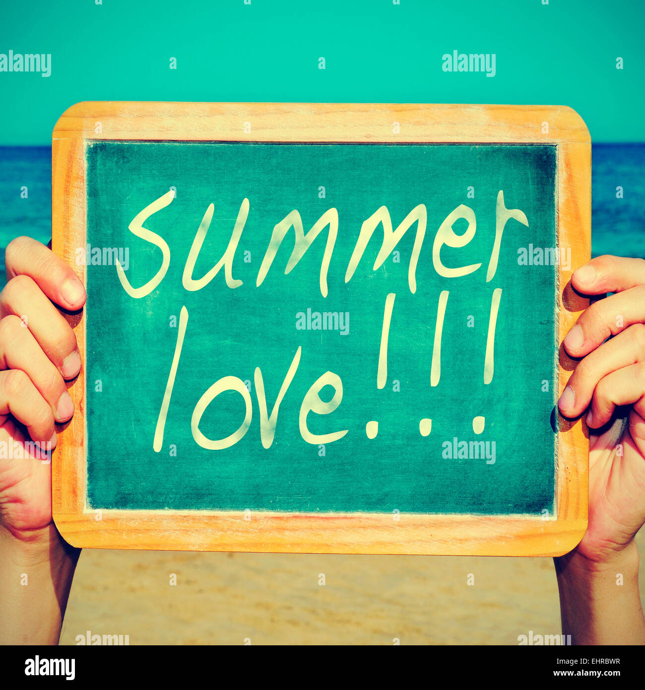 picture of a young man on the beach holding a blackboard with the sentence summer love written on it, with a retro effect Stock Photo