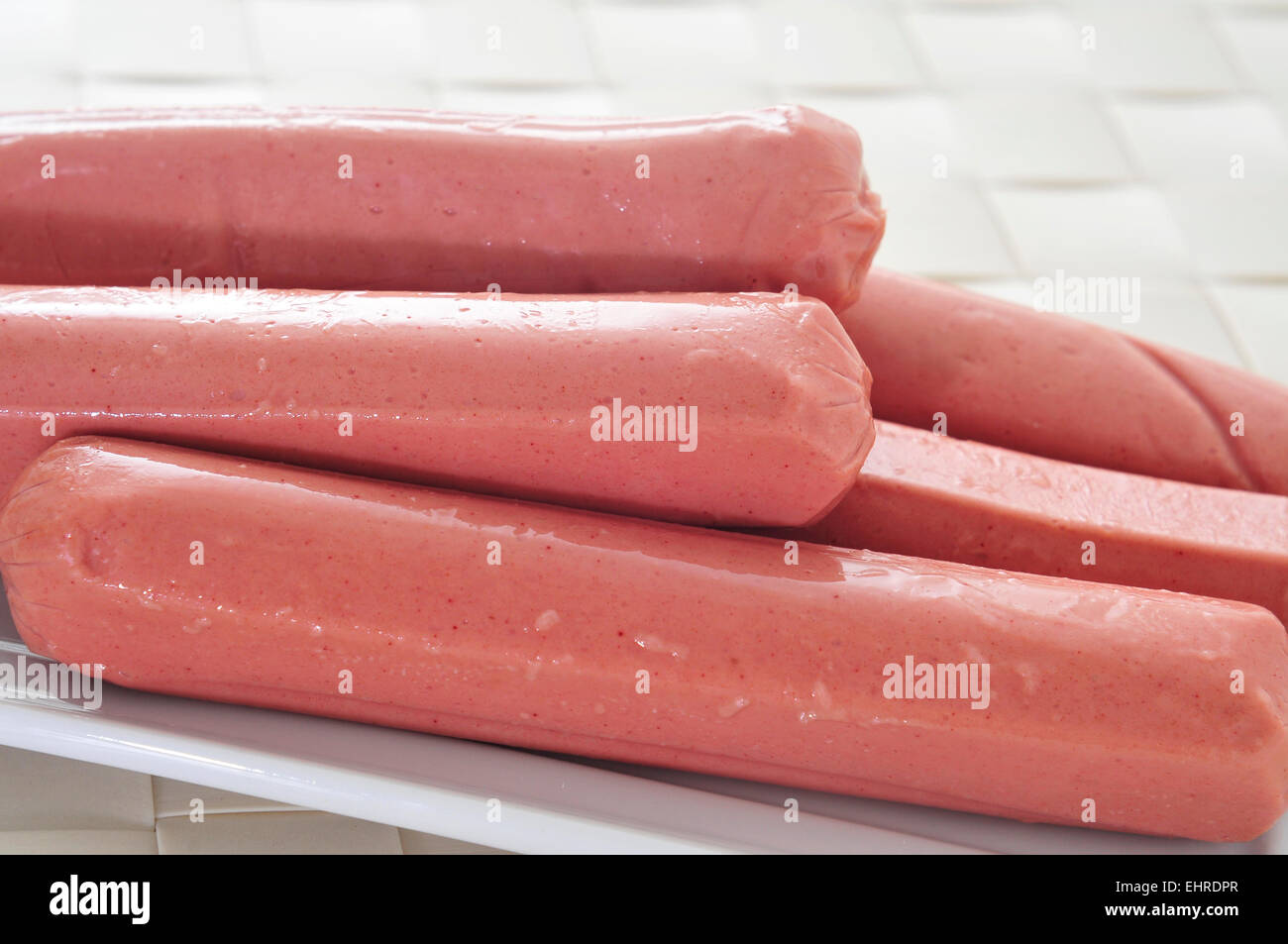 a plate with some raw hot dogs ready to be grilled on a table Stock