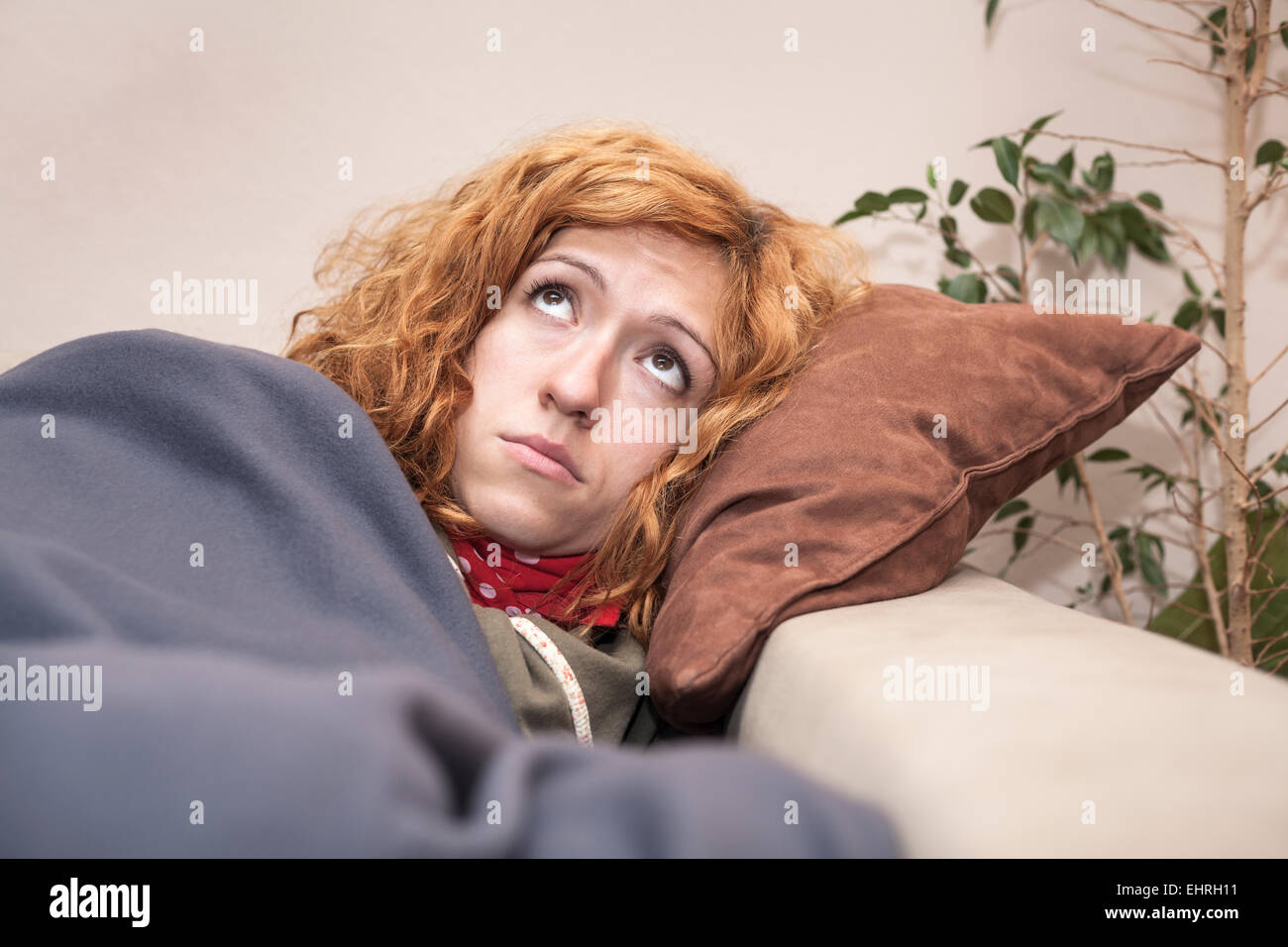 Sad lonely redhead woman looking up and resting on the sofa at home. Stock Photo