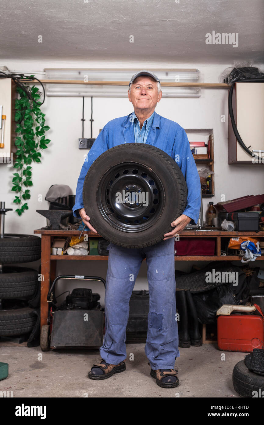 Portrait of happy senior worker changing tire in the garage. Stock Photo