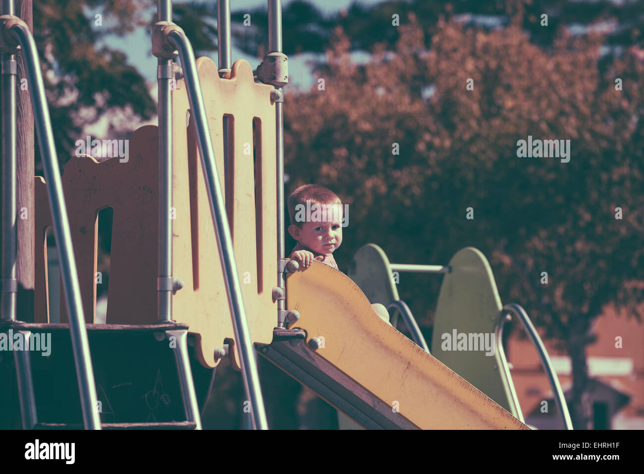Vintage looking photo of a child boy on a slide at children playground. Stock Photo
