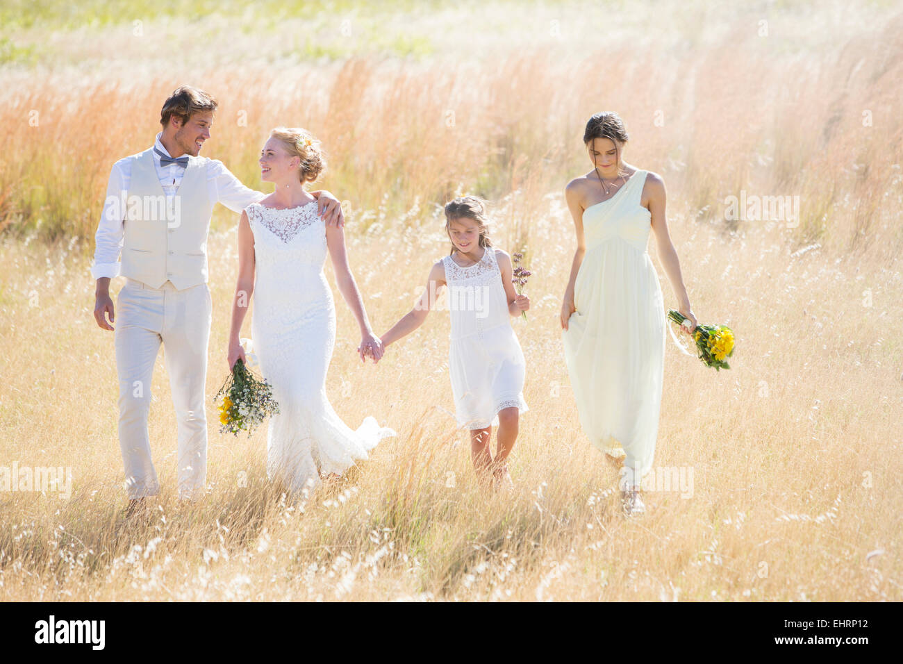 Young couple with bridesmaid and girl walking in meadow Stock Photo