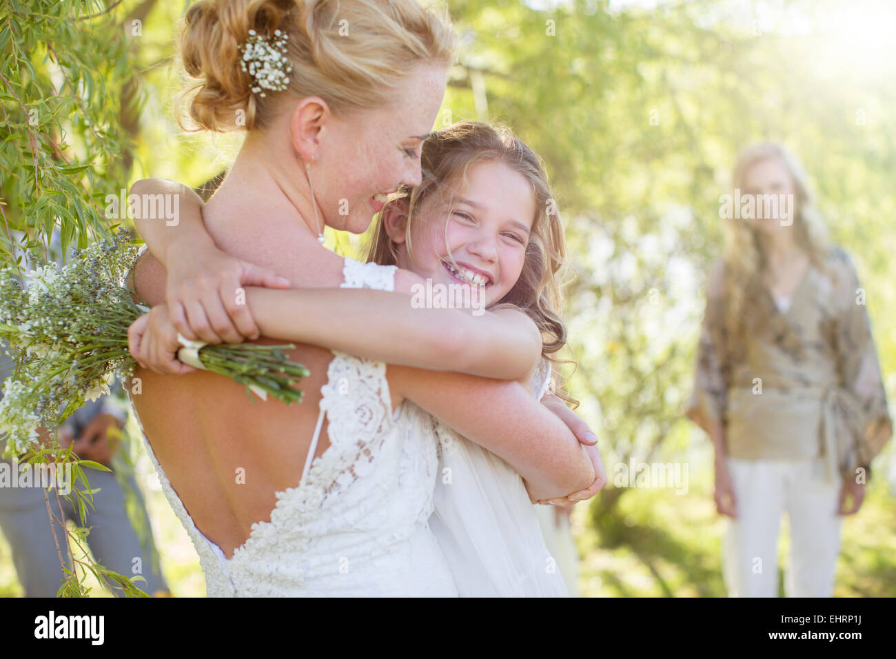Bride embracing bridesmaid at wedding reception in domestic garden Stock Photo