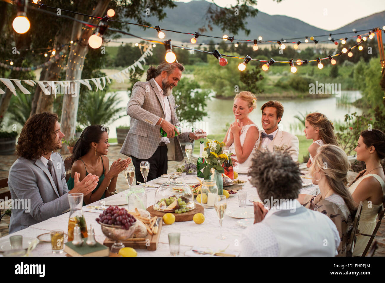 Best man pouring champagne into flutes during wedding reception in domestic garden Stock Photo