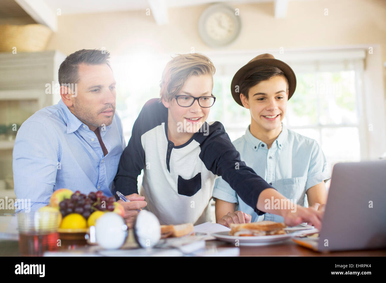 Teenage boys with father using laptop in dining room Stock Photo