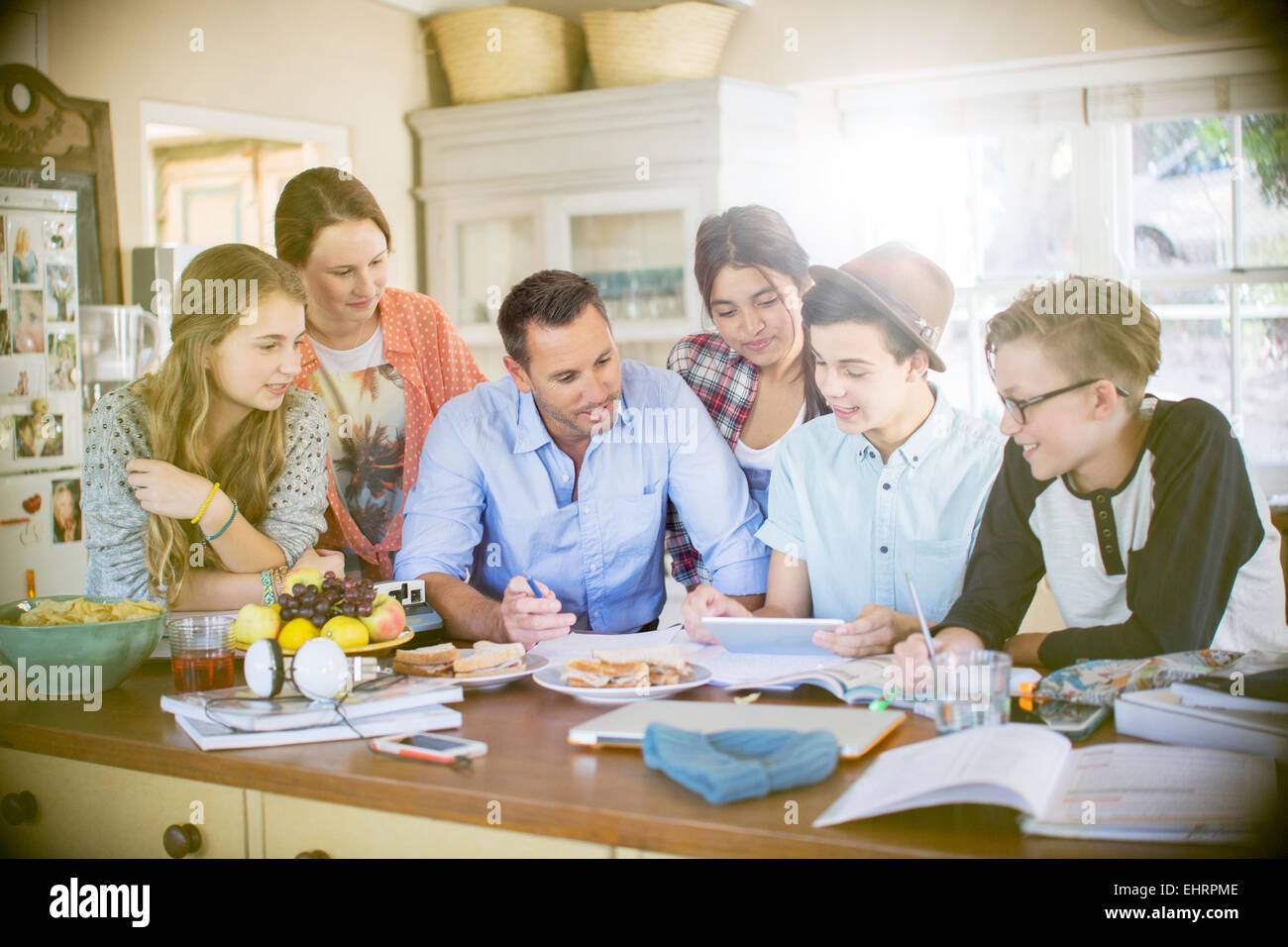 Group of teenagers with mid adult man using digital tablet at table in dining room Stock Photo